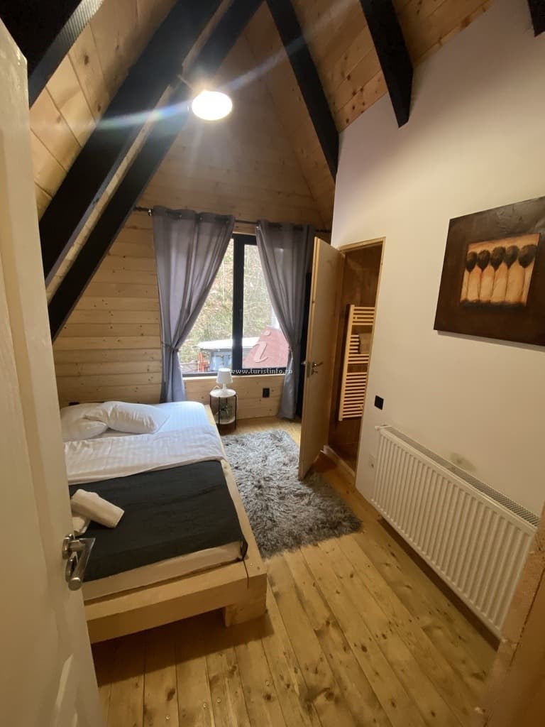 Dormitor matrimonial cu fereastră, draperii închise, radiator port-prosop și un tablou pe peretele alb.