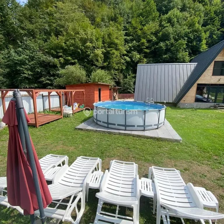Piscina rotundă pe gazon, cu șezlonguri albe și umbrelă alături.