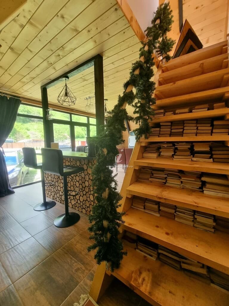 Scara din lemn a cabanei, cu cărți stivuite sub fiecare treaptă, lângă blatul-bar placat cu felii de lemn.