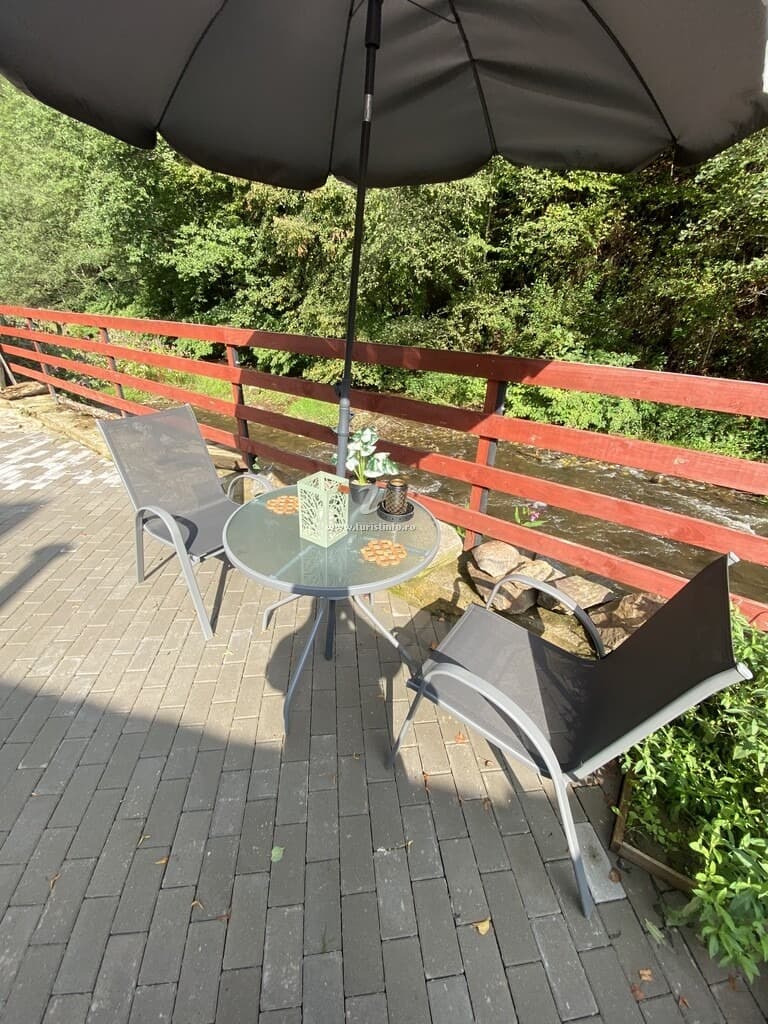 Masă și scaune pe terasa pavată, lângă balustrada cărămizie și lemnele de foc stivuite.