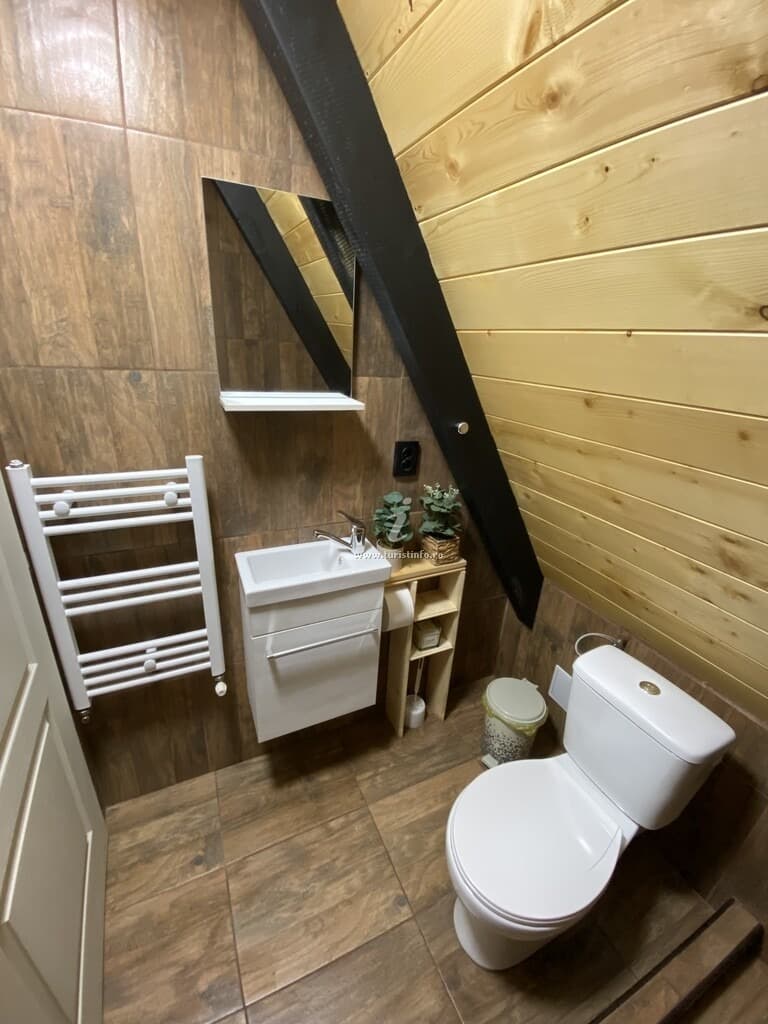 Baie compactă cu lavoar, radiator port-prosop și perete placat cu gresie imitație lemn, sub panta acoperișului.