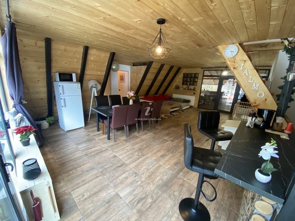 Bucătăria și zona de luat masa, cu scaune de bar la blat și scaune negre la masă.