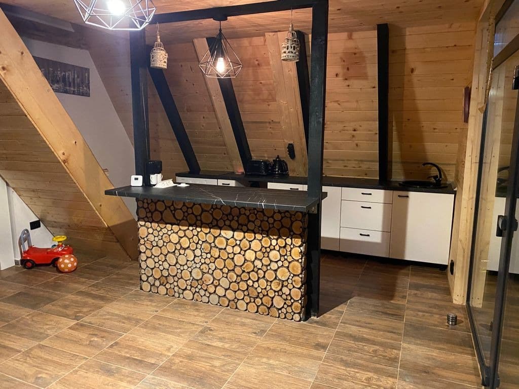 Bucătăria cu blat-bar placat cu felii de lemn tăiate transversal, corpuri albe și lămpi industriale suspendate.