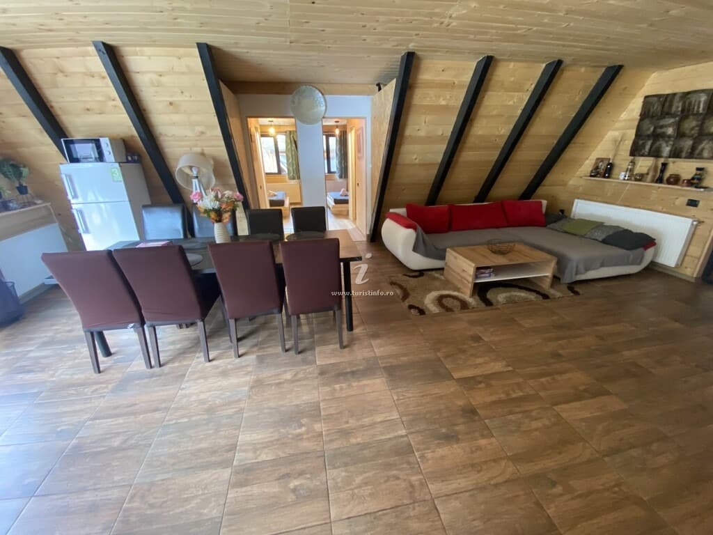 Zona de living cu canapea de colț, banchetă roșie și masă de dining, sub structura în A a cabanei.