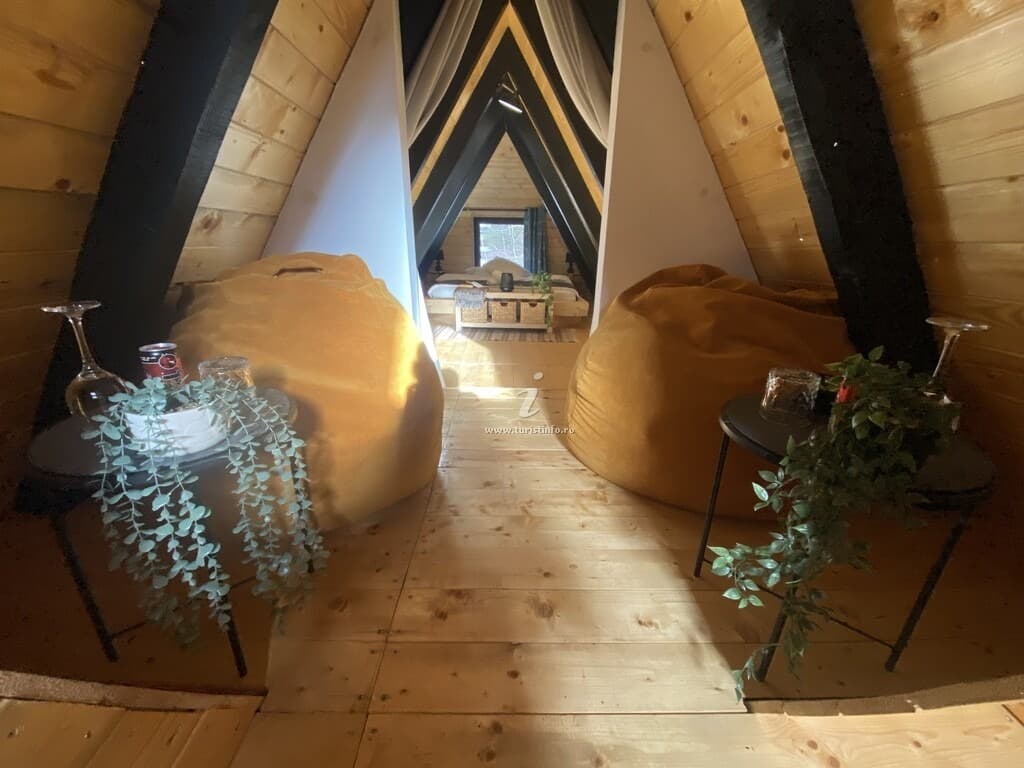 Mezaninul de sub coama acoperișului, cu două fotolii puf și măsuțe, încadrat de structura în A.